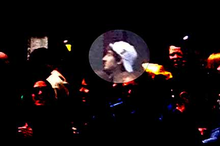 Suspect in the gangster-looking white hat looks through the crowd.